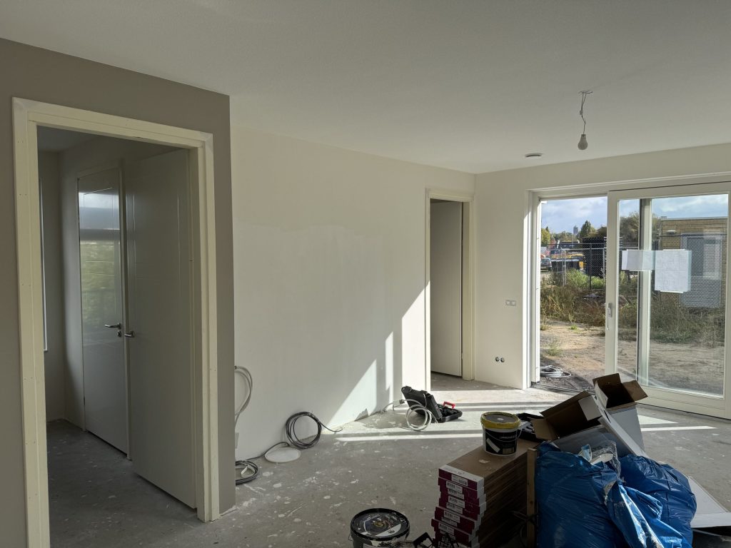 Woonkamer tijdens de afwerking met kale wanden, verfemmers en zon door de schuifpui