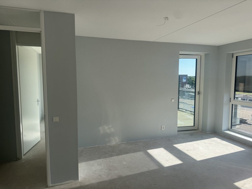 Kamer met lichtgrijze wanden, een betonvloer en een deur naar het balkon