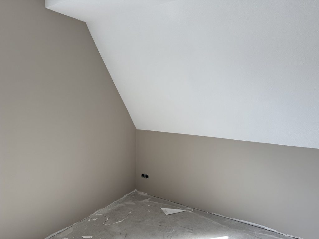 Zolderkamer met een witte schuine wand boven rechte wanden in een warme grijstint