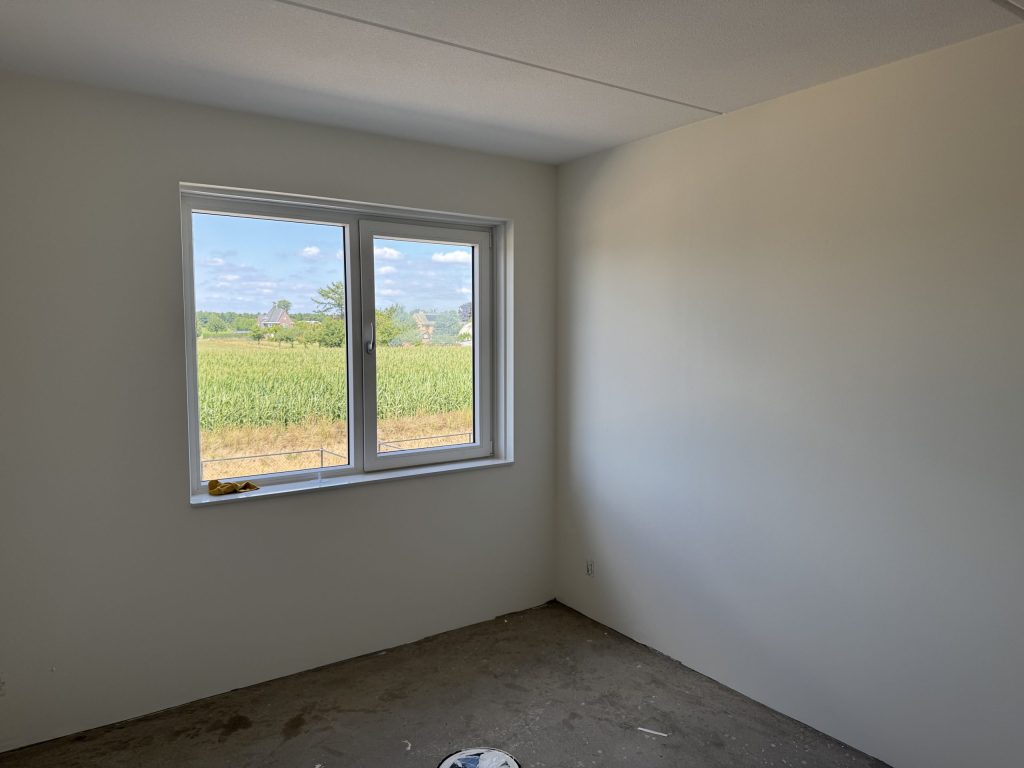 Lege kamer met strakke witte wanden en een raam dat uitkijkt op een maisveld