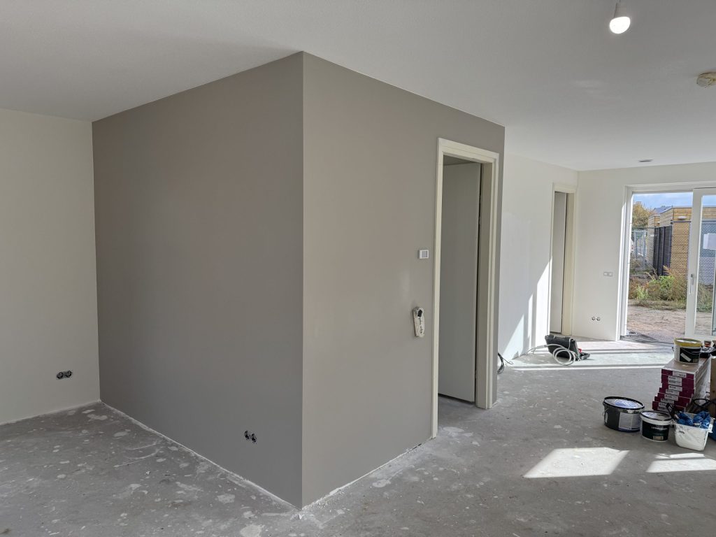 Open woonruimte met een pas gesausde grijze wand, verfemmers en dozen op de betonvloer