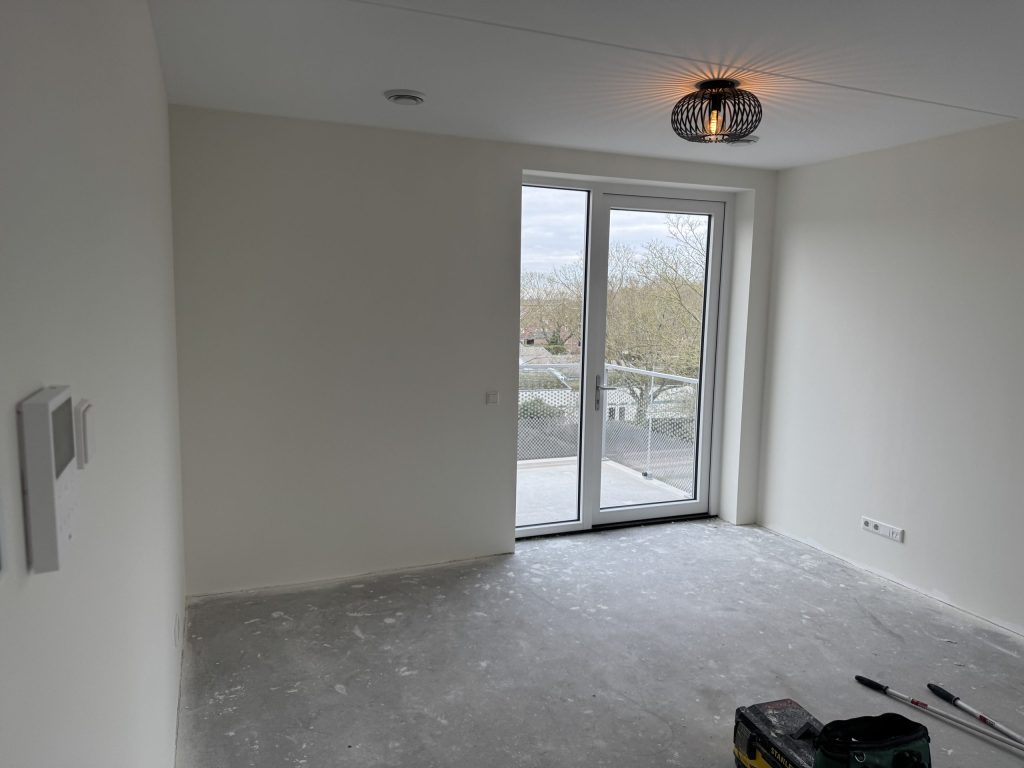 Lichte kamer met witte wanden, een plafondlamp en openslaande deuren naar het balkon