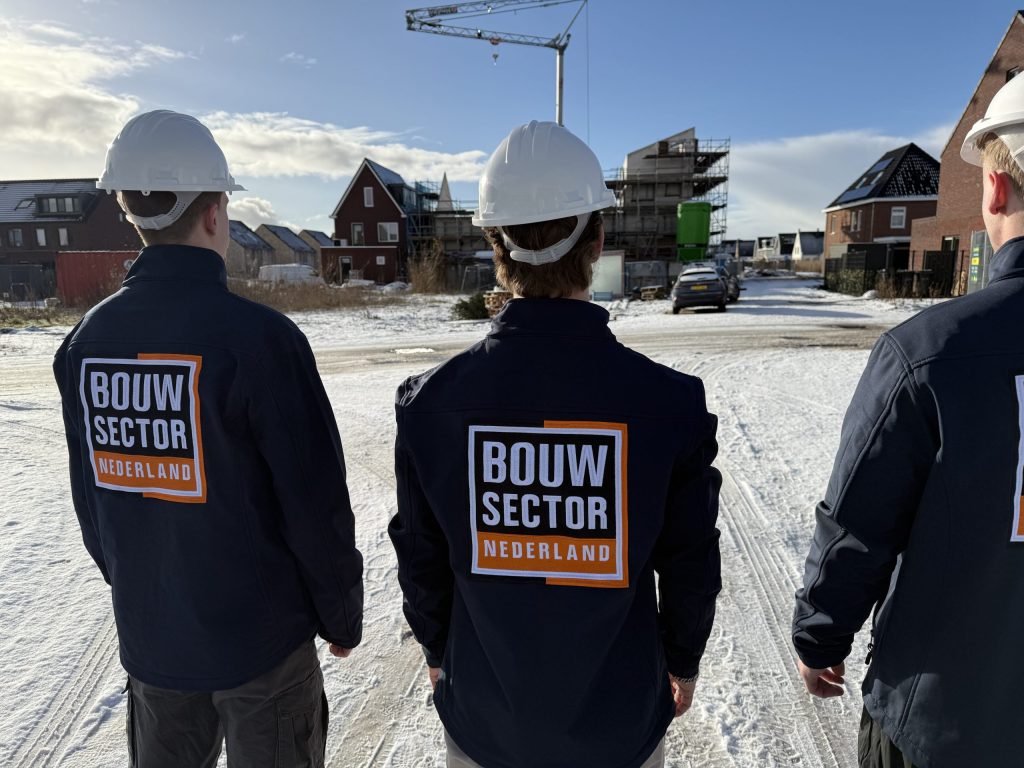 Drie vakmensen van Bouwsector Nederland met witte helm kijken naar een woning in de steigers